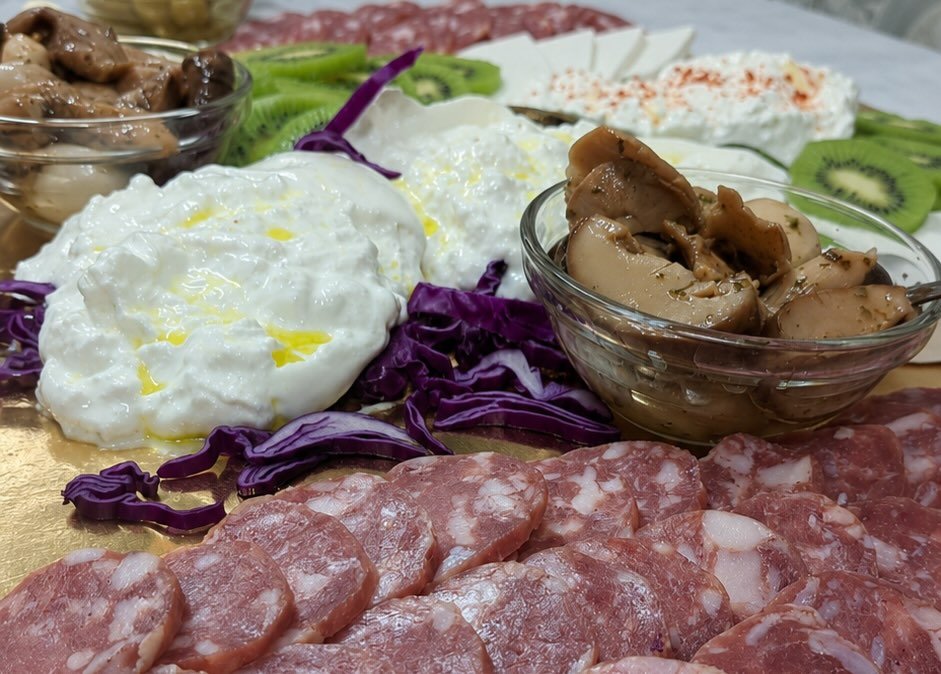 Vassoio dorato con salame a fette, stracciatella all'olio, ricotta, cavolo viola, kiwi e funghi in ciotole di vetro