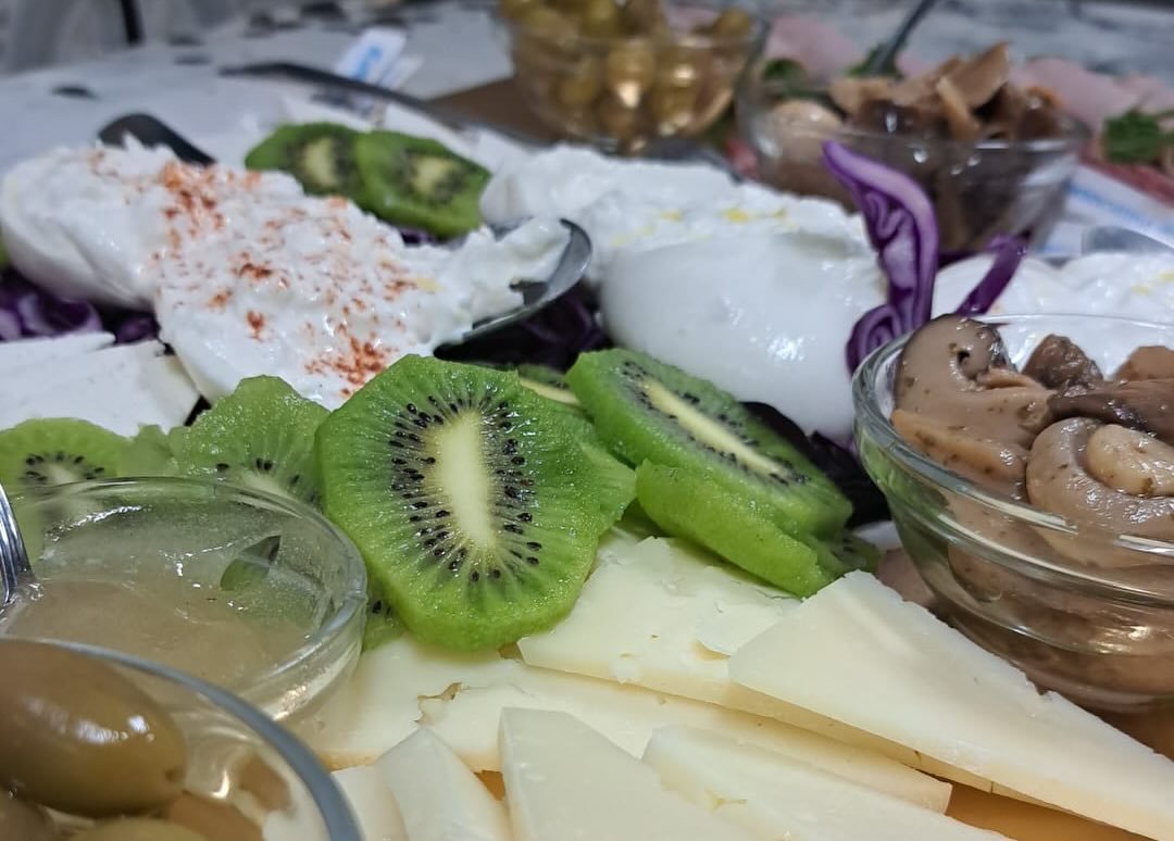 Tagliere con burrata alla paprika, fette di kiwi, formaggio a scaglie, olive verdi, funghi e cavolo viola in ciotoline di vetro